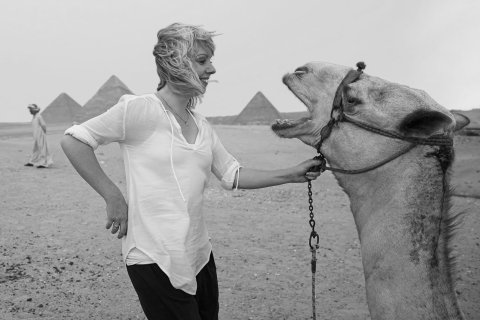 Eine Frau und ein Kamel schauen sich an vor den Pyramiden von Gizeh und Sphinx